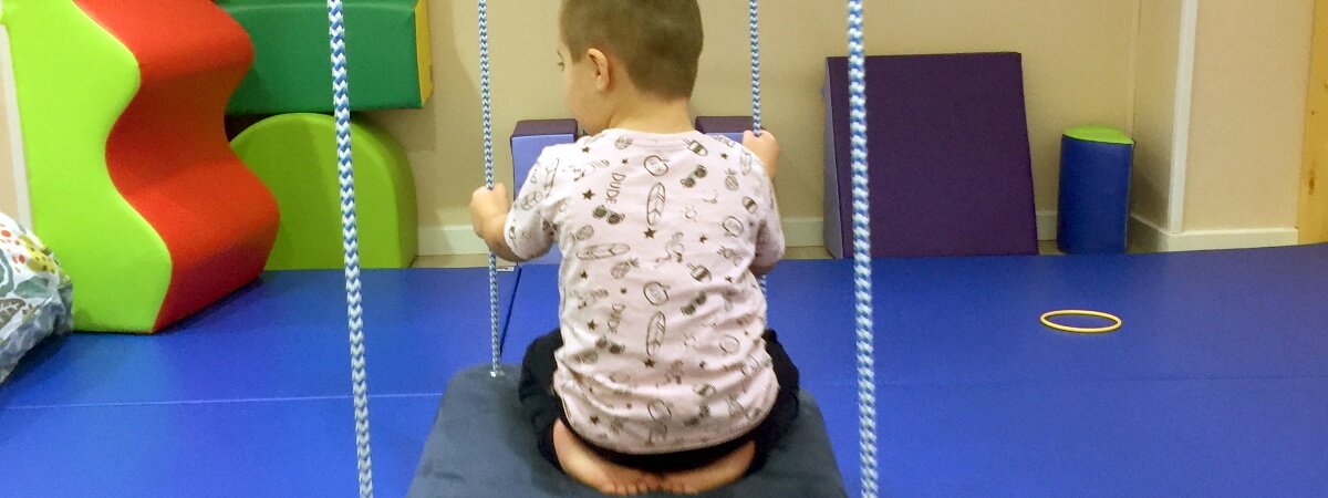 Niño de espaldas sentado en una gran plataforma colgante durante una sesión de terapia ocupacional infantil