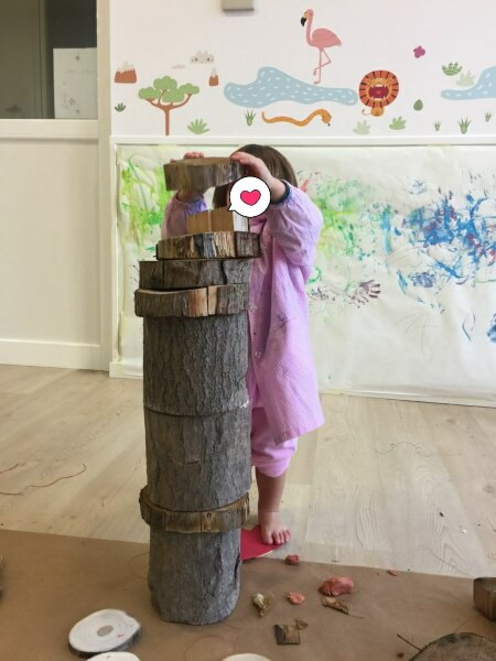 Niño creando una torre con trozos de tronco de árbol cortados. La torre llega a la altura de su cabeza. Esta actividad está diseñada para ser un desafío justo.
