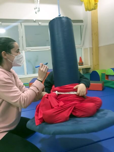 La terapeuta ocupacional de enDARA Marta, con mascarilla, sujeta una cuchara azul con su mano en dirección a la boca de un niño con problemas de integración sensorial.