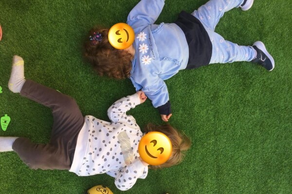 Dos niñas tumbadas en el suelo boca arriba sobre un césped. El contacto con la naturaleza es uno de los puntos principales del método Reggio-Emilia