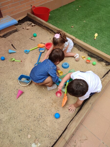 El juego en la escuela facilita el periodo de adaptación de los niños. En esta foto hay dos niños y una niña jugando en la arenera de la escuela infantil enDARA
